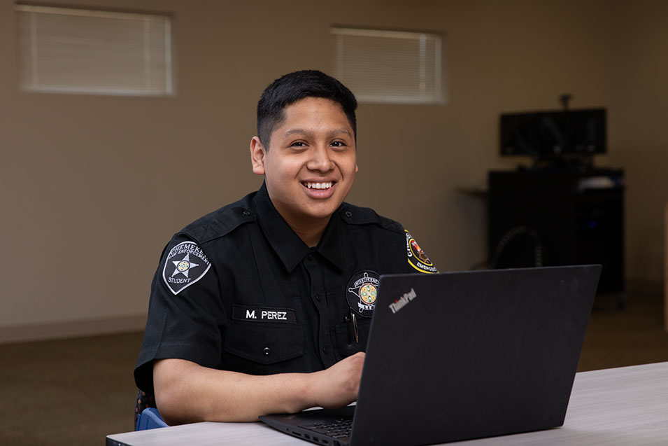 A Criminal Justice student in uniform using a laptop
